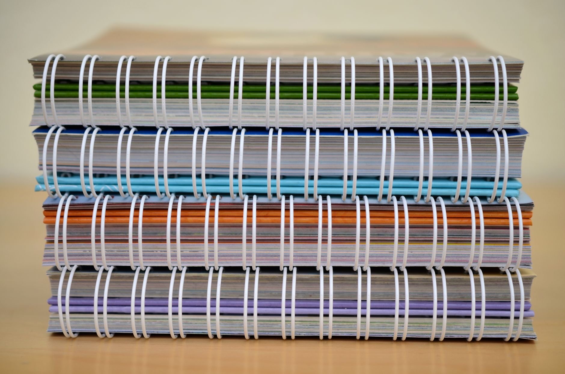 A stack of colorful spiral-bound notebooks placed on a wooden table, showcasing various colors and designs.